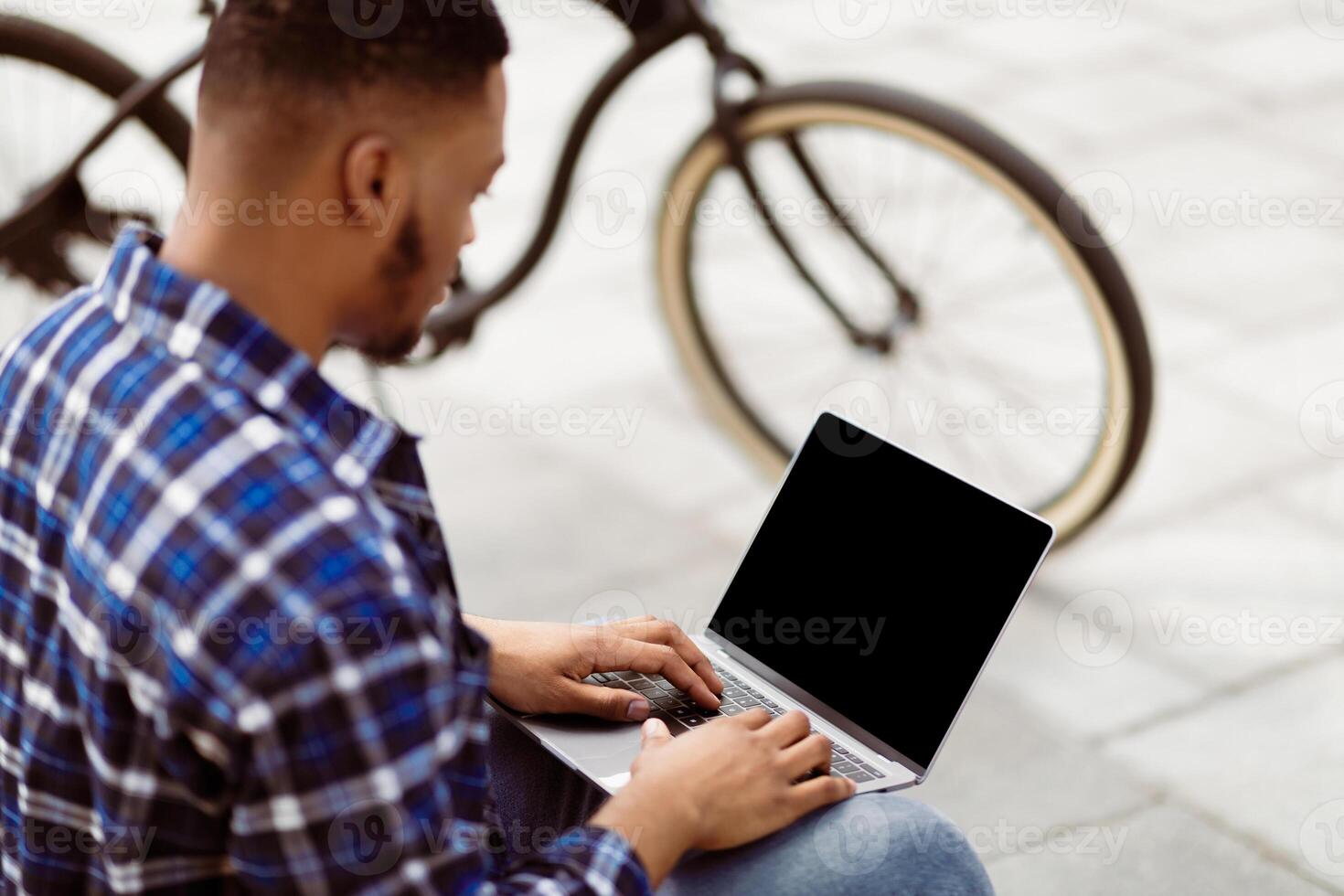 Mock up image of black man using and typing on laptop computer with blank desktop screen on the street photo