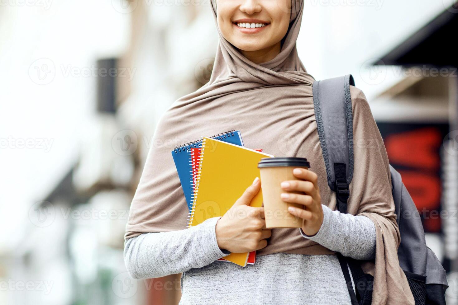 Happy muslim girl holding books and coffee to go, going to college, panorama with copy space photo