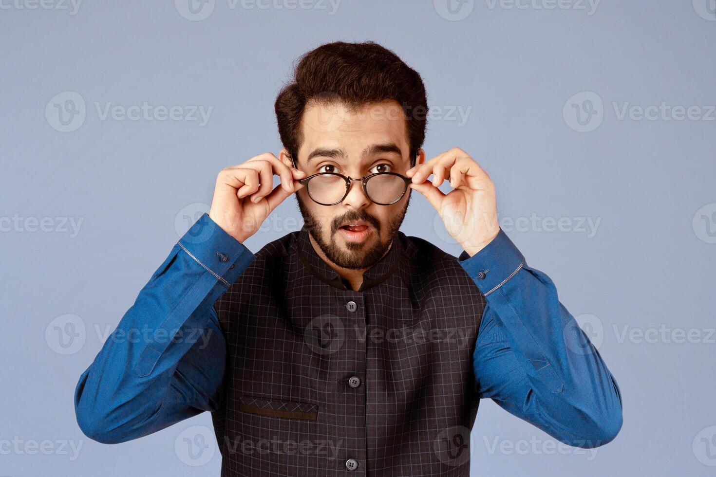 Attractive Indian man taking off his glasses in surprise on lilac background photo