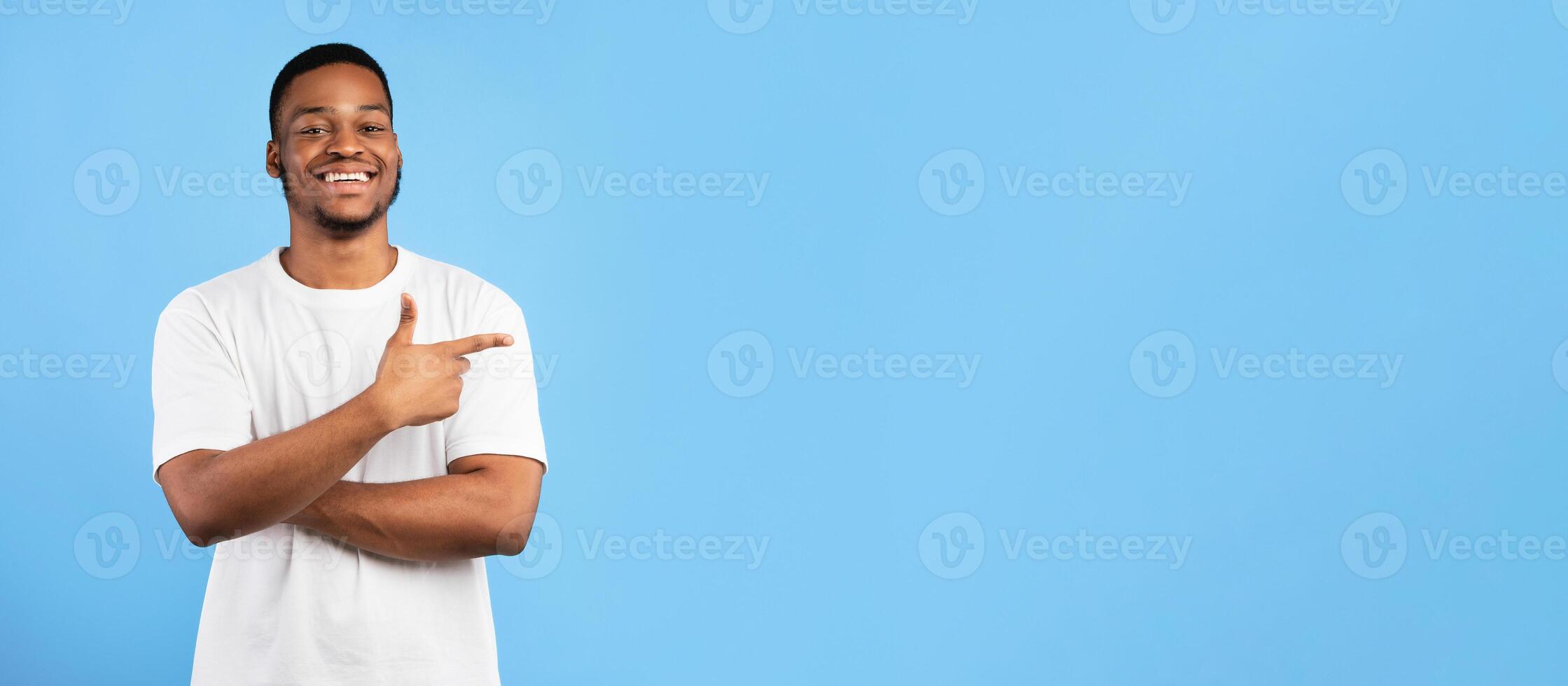 Look There. Positive African American Guy Pointing Finger Aside At Blank Space Standing On Blue Background In Studio. Panorama photo