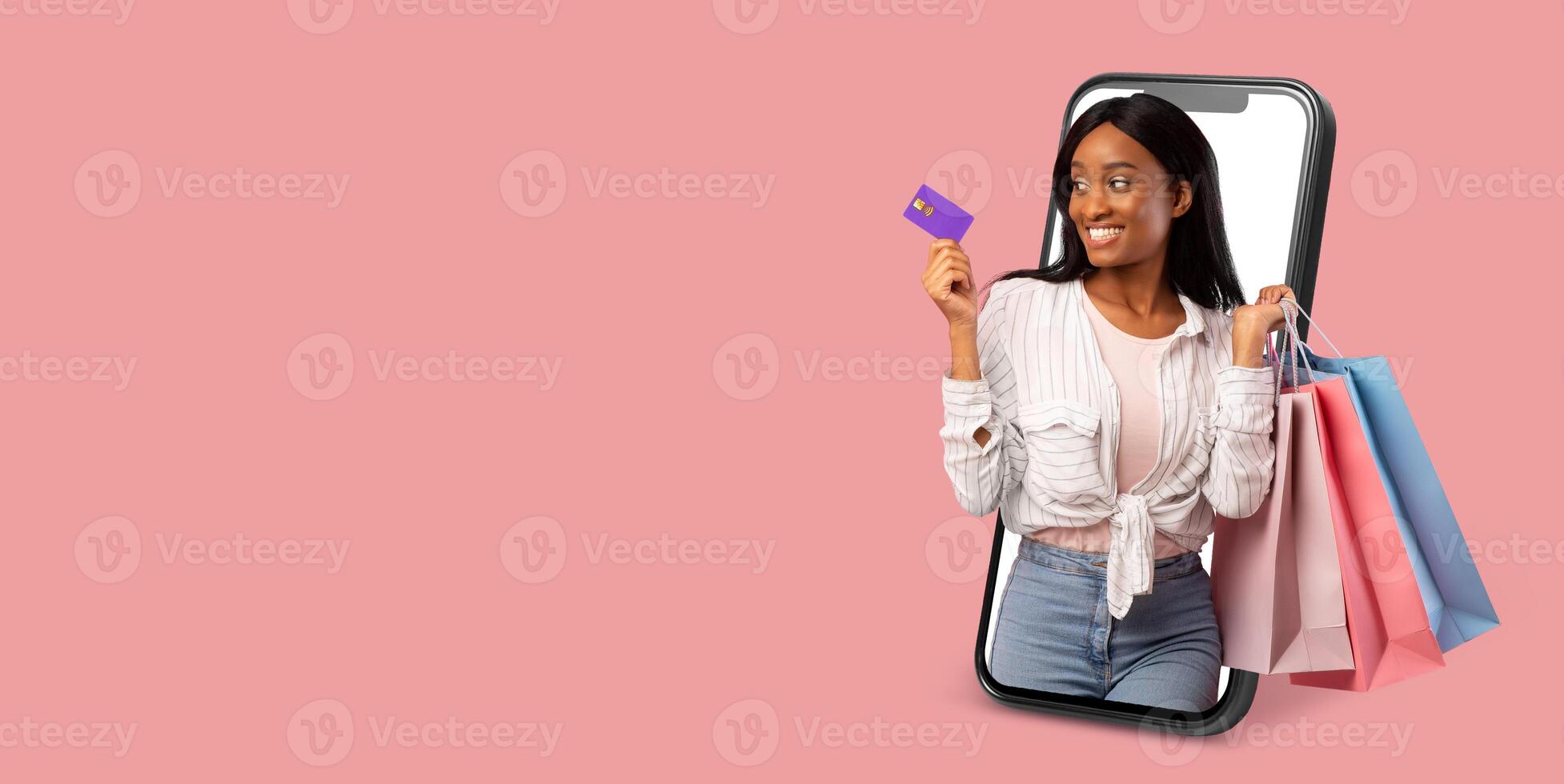 A buyer happily interacts with a smartphone displaying an online store. She holds shopping bags in one hand and a credit card in the other, ready to make her purchase. photo