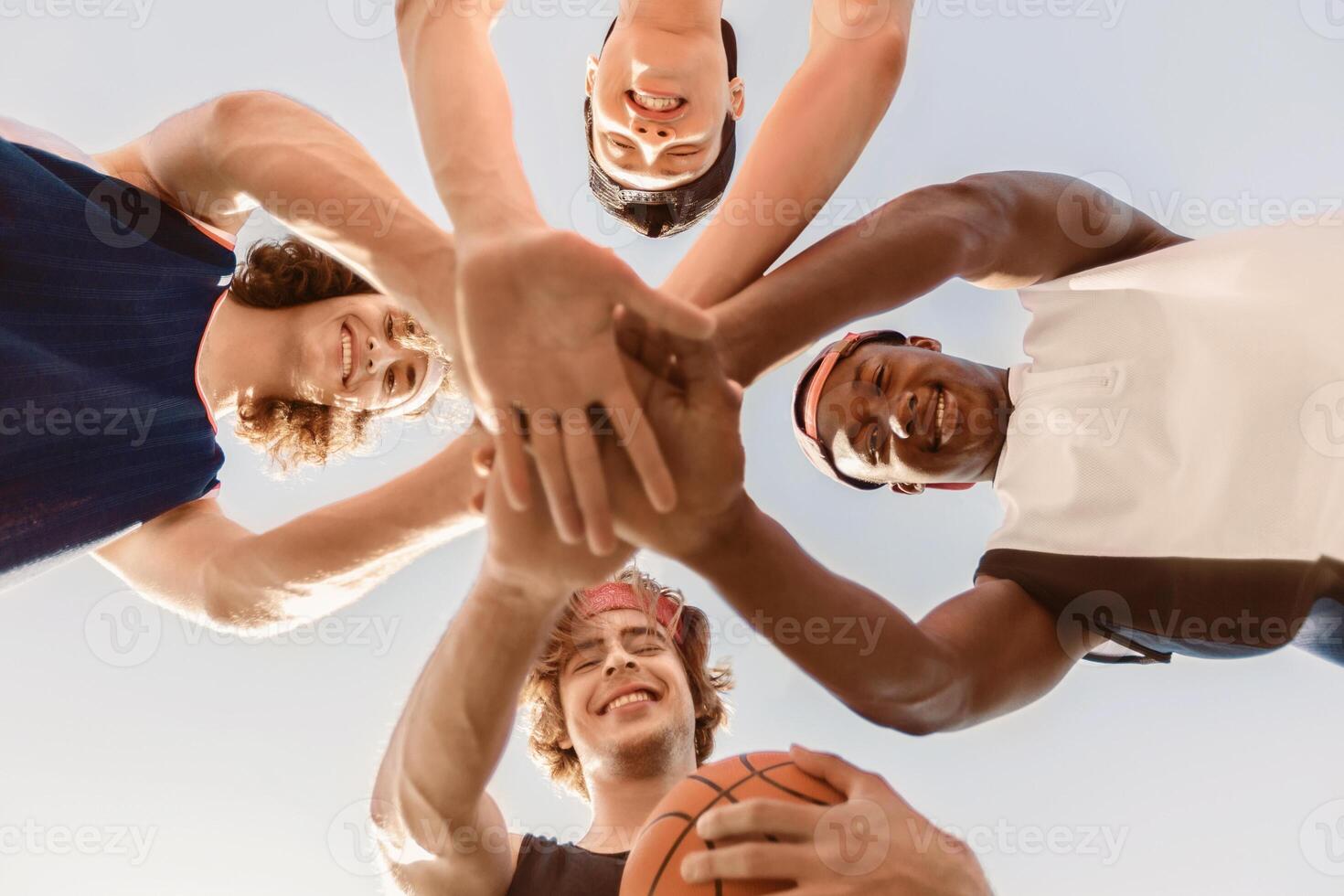 Bottom view of happy multiracial basketball team putting their hands together in unity before game outdoors photo