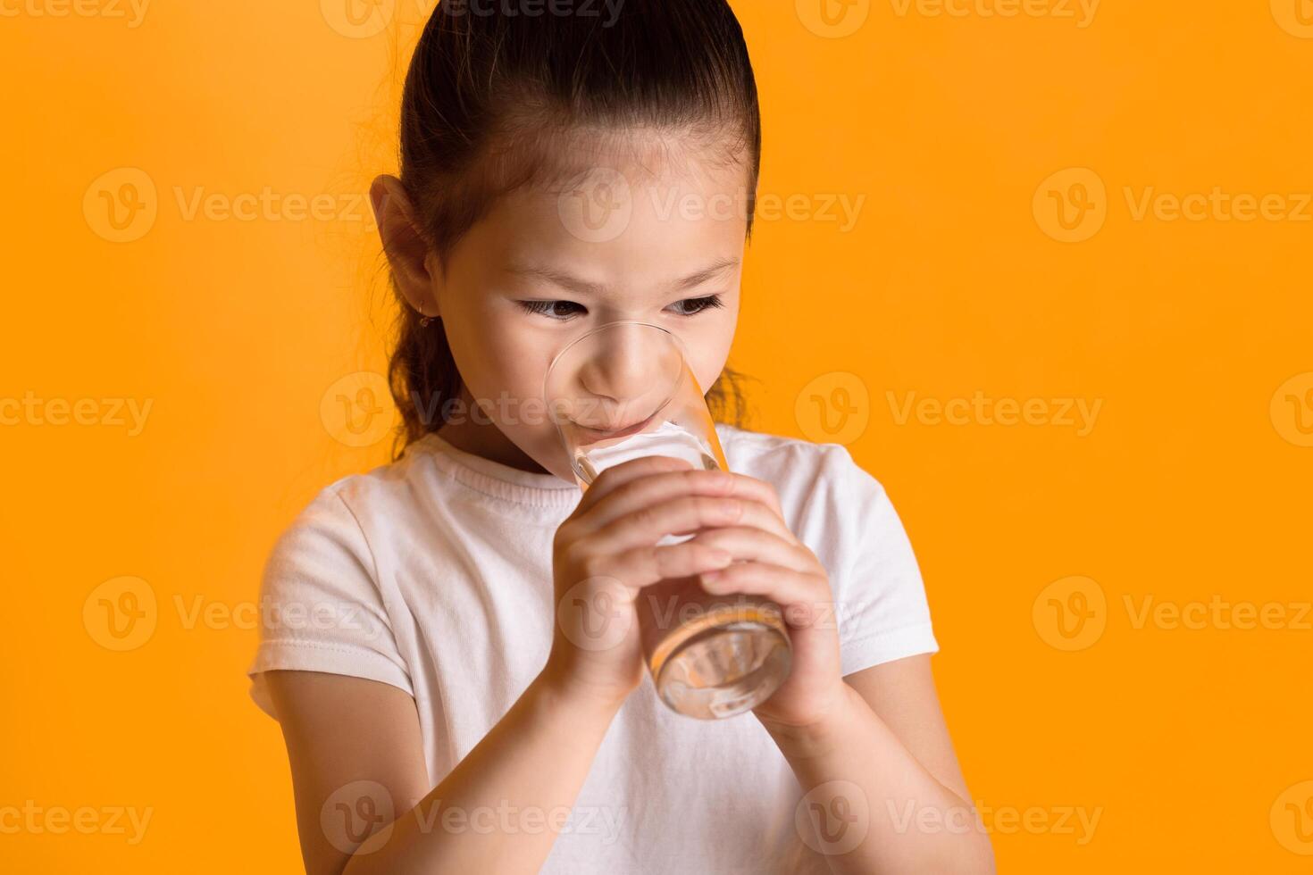 Stay Hydrated Concept. Close up portrait of small asian girl drinking fresh water, isolated over yellow wall, copy space photo