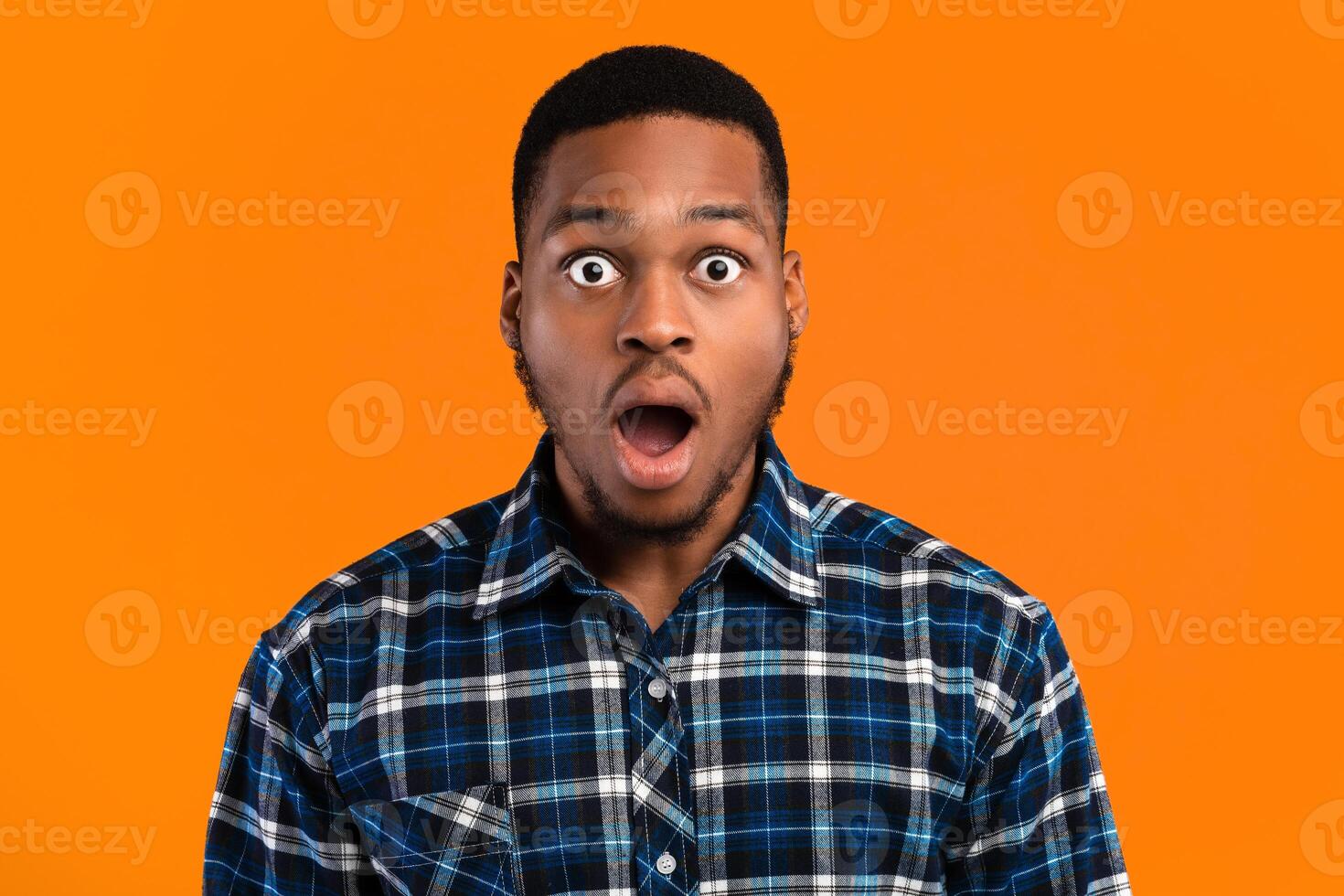 Shocked African Man Looking At Camera In Amazement Posing With Opened Mouth Standing On Yellow Background. Studio Shot photo