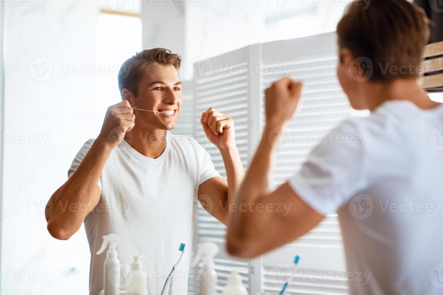 Taking Care Of Teeth. Portrait of handsome man using dental floss looking in mirror, view over the shoulder photo