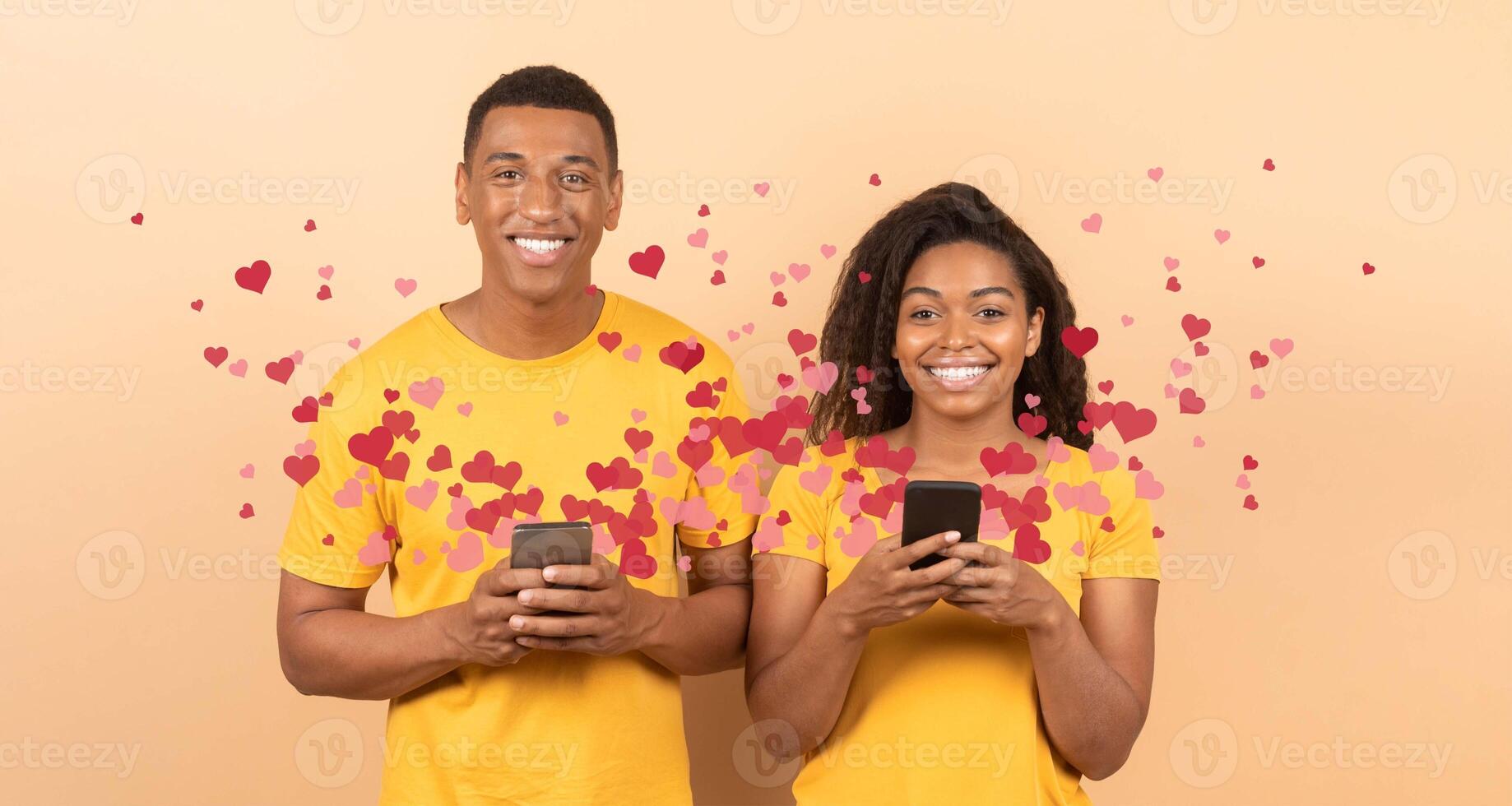 A joyful couple stands together, each holding a smartphone. They send affectionate messages to each other filled with love for St. Valentine's Day, surrounded by playful heart graphics. photo