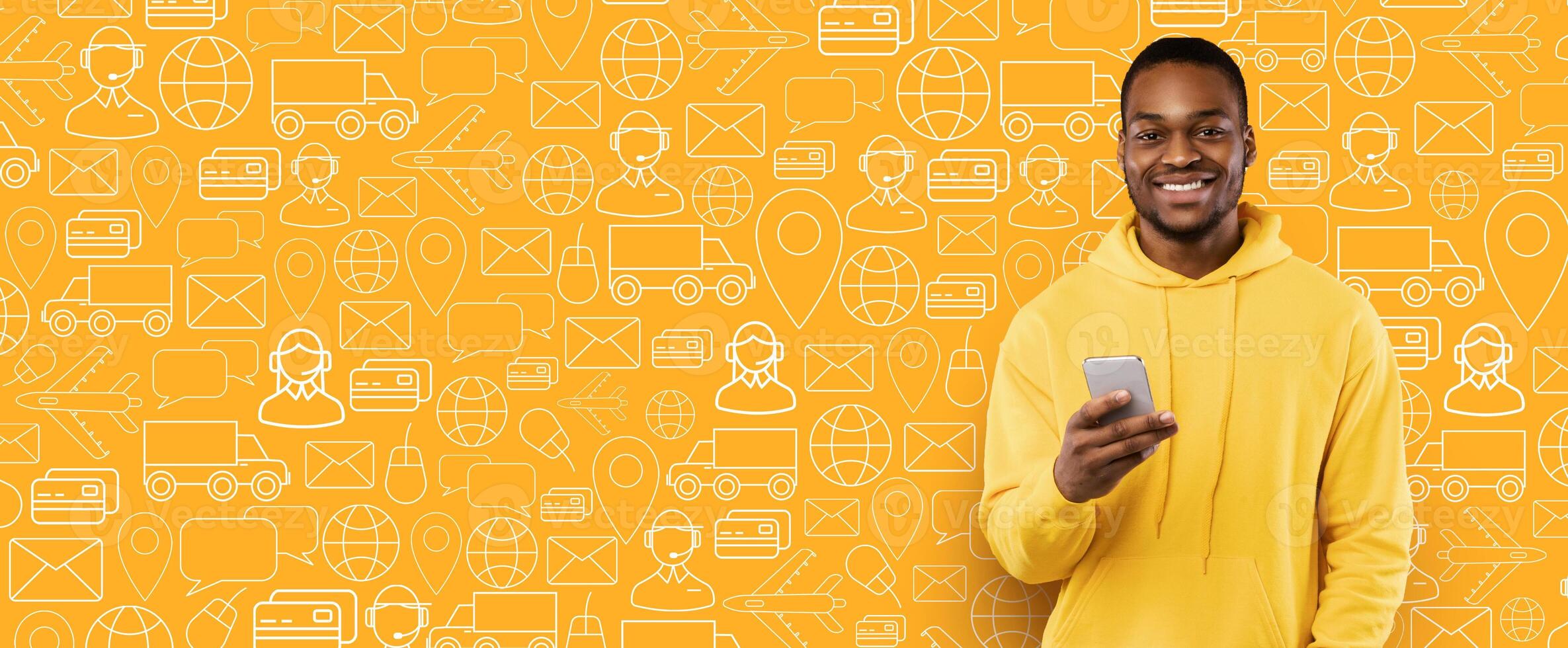 A cheerful buyer stands against a vibrant yellow background filled with delivery and shopping icons. He holds a smartphone, ready to complete an online purchase for a service. photo