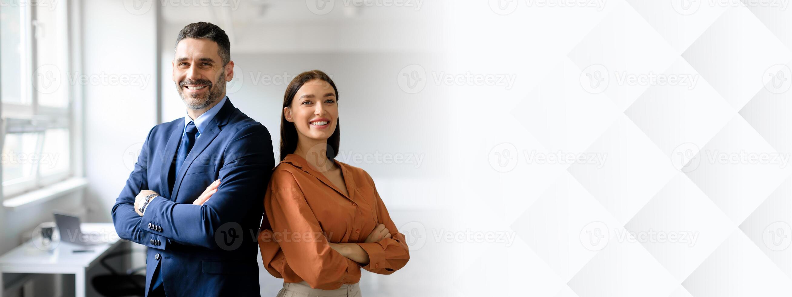 Successful happy businessman and businesswoman standing back to back with arms crossed and smiling at camera, office interior. Partnership concept, copy space photo
