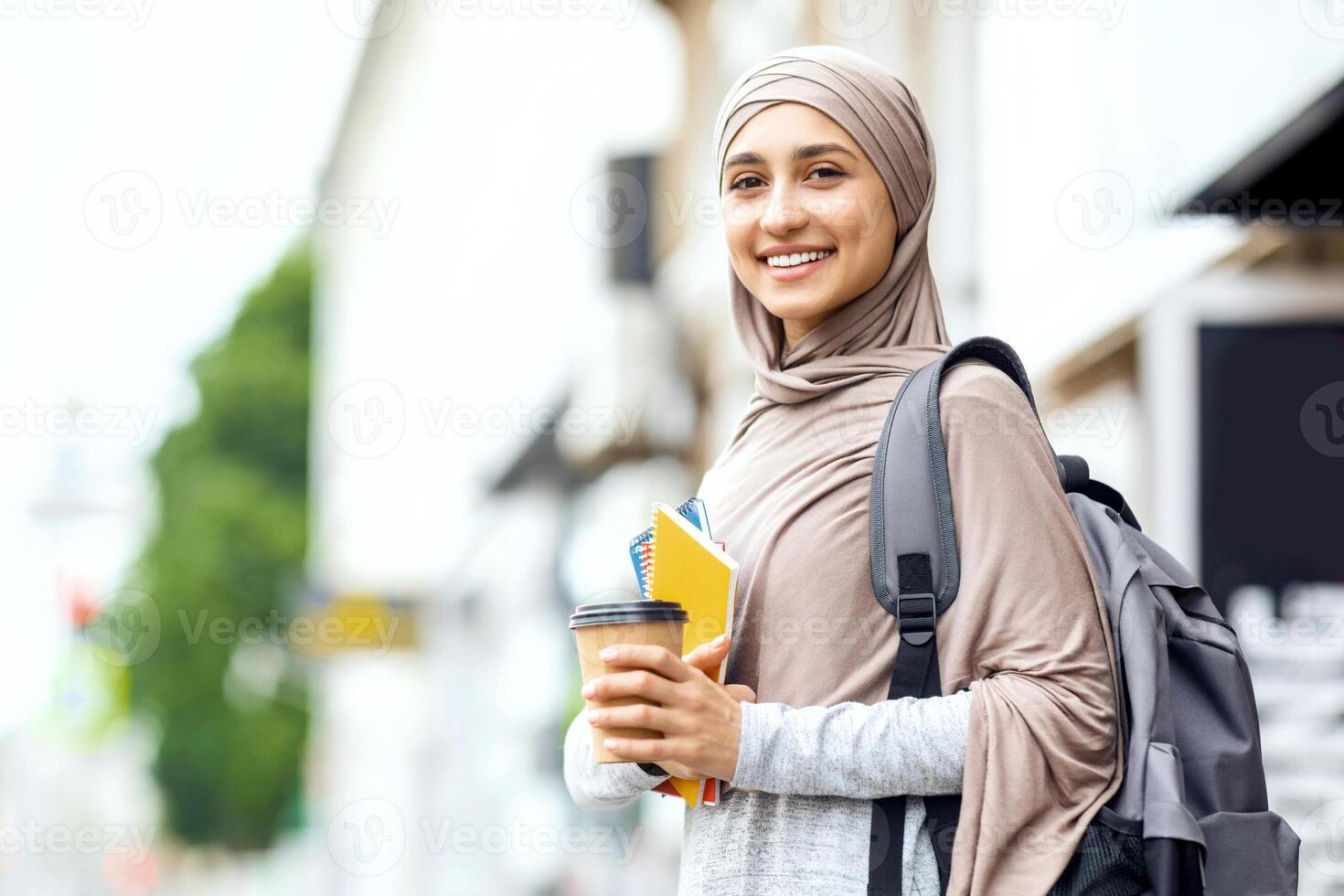 Smiling muslim girl student drinking coffee on street before studying, copy space photo