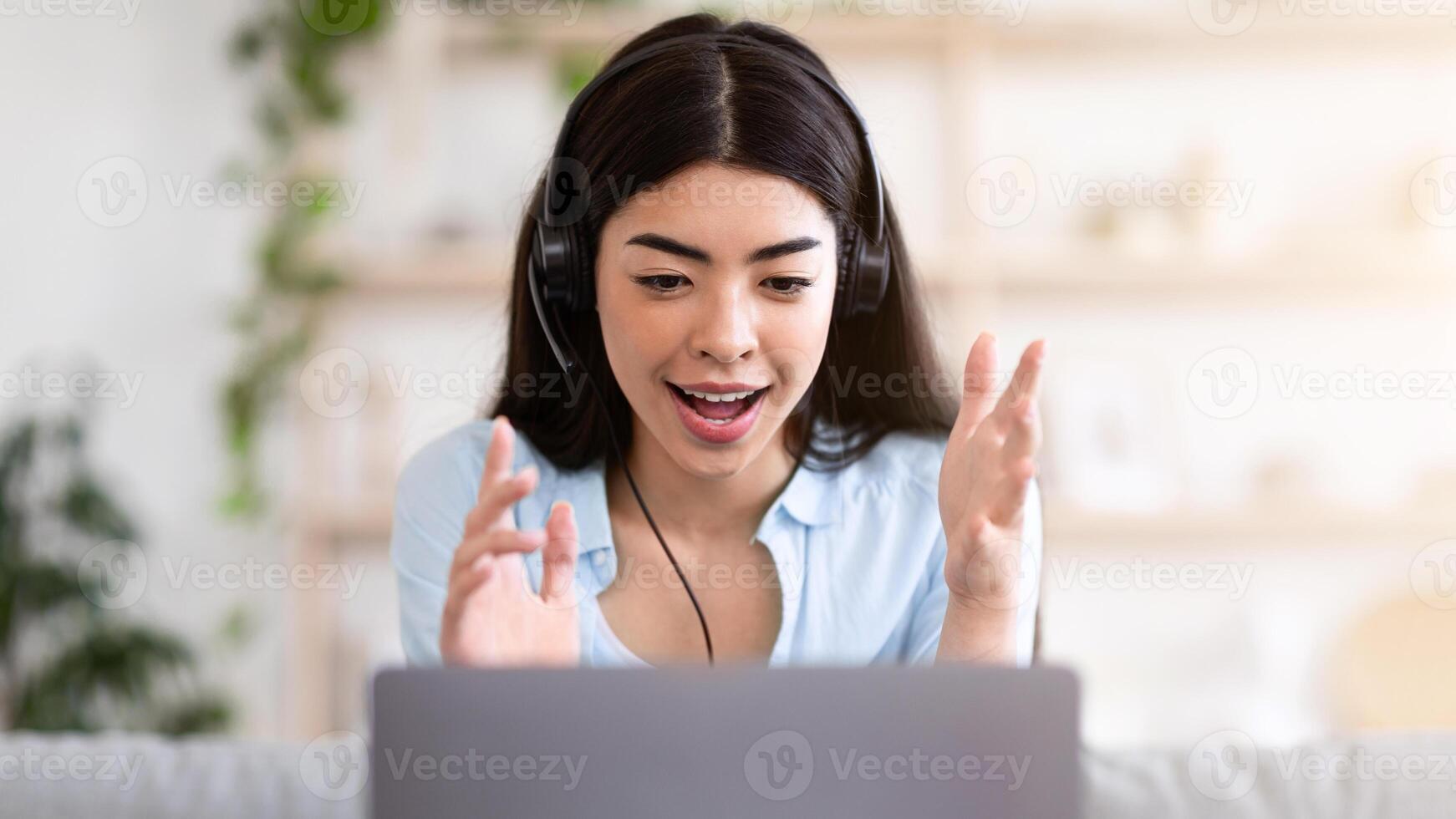 Conference. Asian girl having web call on laptop computer at home, speaking at camera while sitting on couch in living room, free space photo