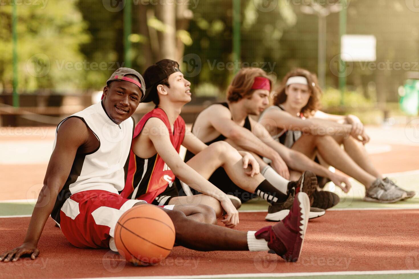 Black basketball player with his diverse team relaxing at outdoor court after championship, free space. Young multiracial sportsmen communicating before game, discussing their tactics photo