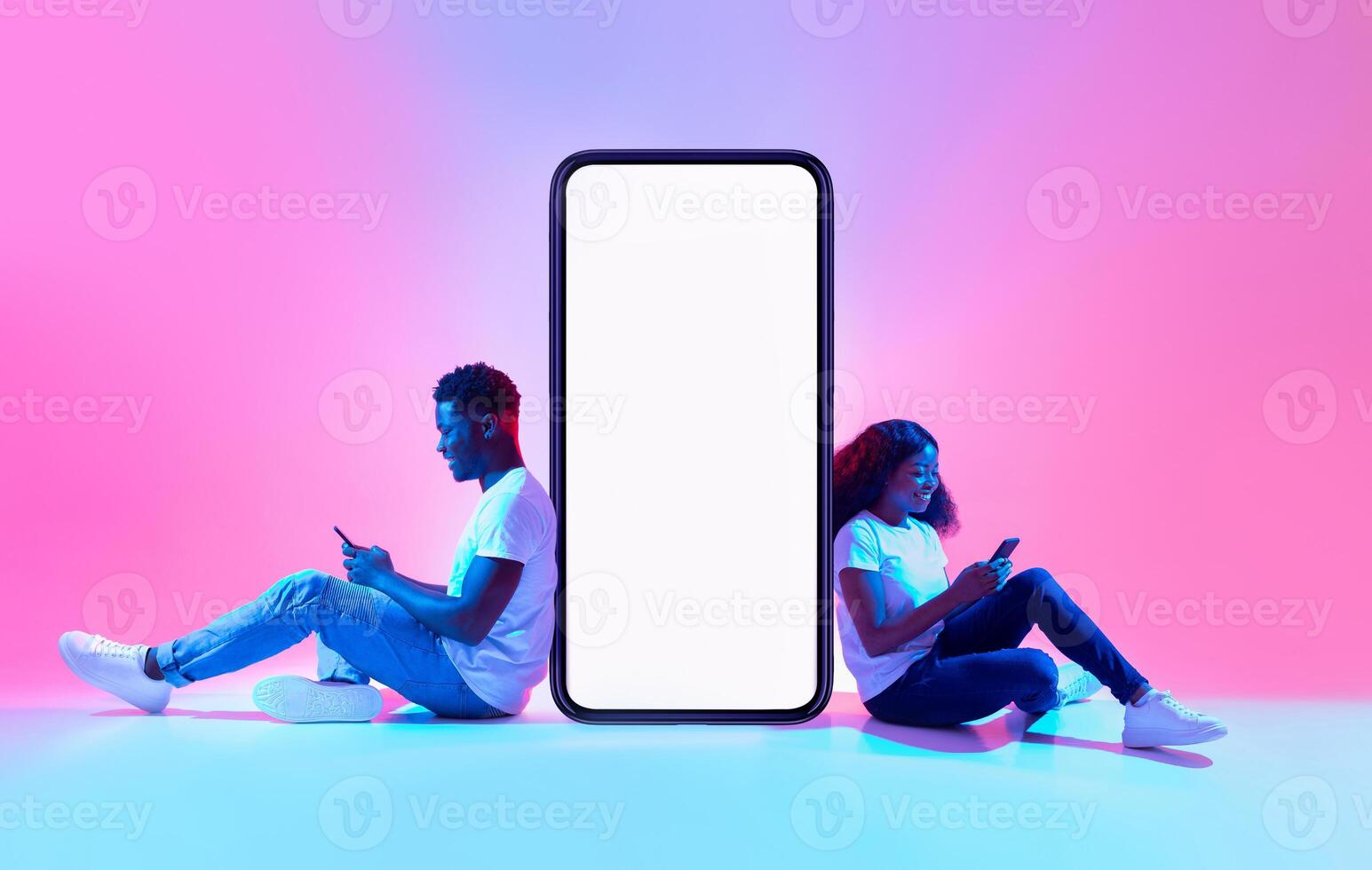 Cool mobile app. African American couple sitting near big smartphone with mockup, using modern gadgets, advertising new application or website, promoting your product or service in neon light photo