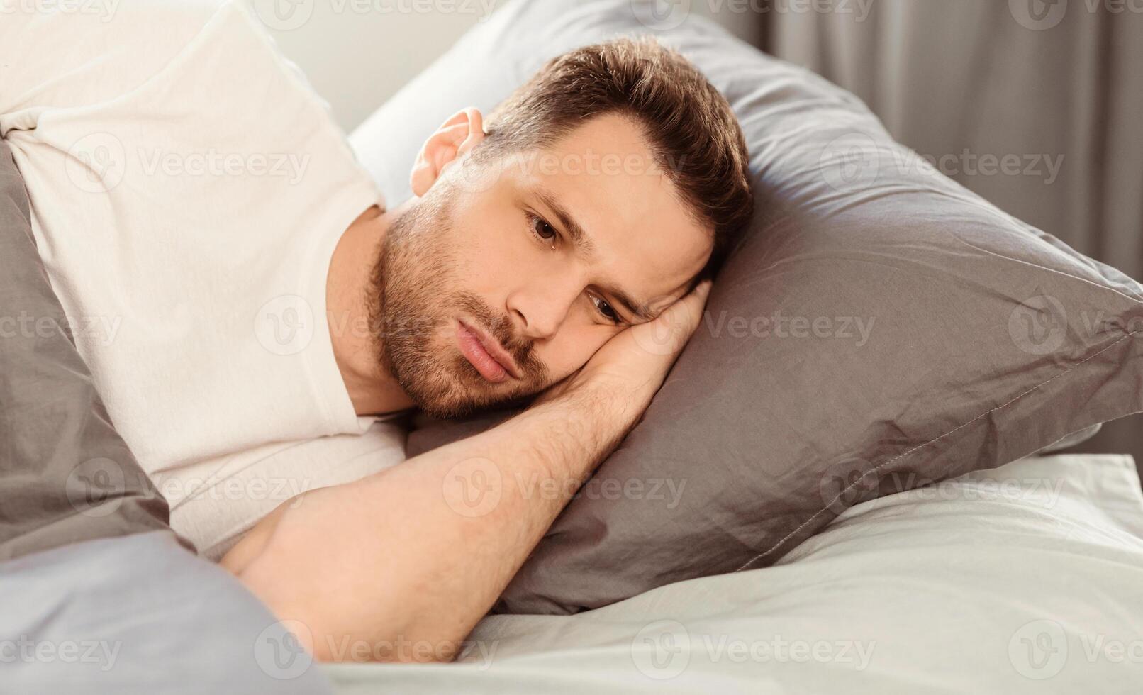 Male Depression Concept. Apathetic Man Having Insomnia Thinking About Problems Lying In Bed At Home. Copy Space photo