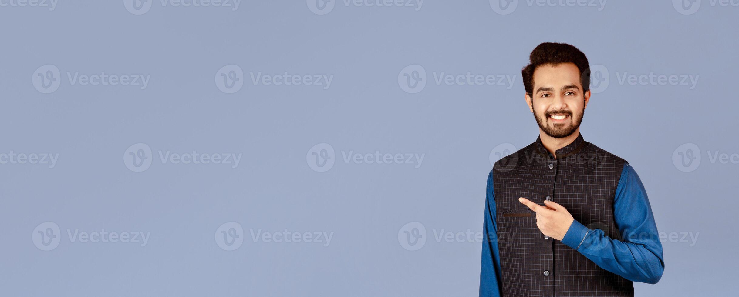 Handsome young Indian man smiling and pointing aside on lilac background photo