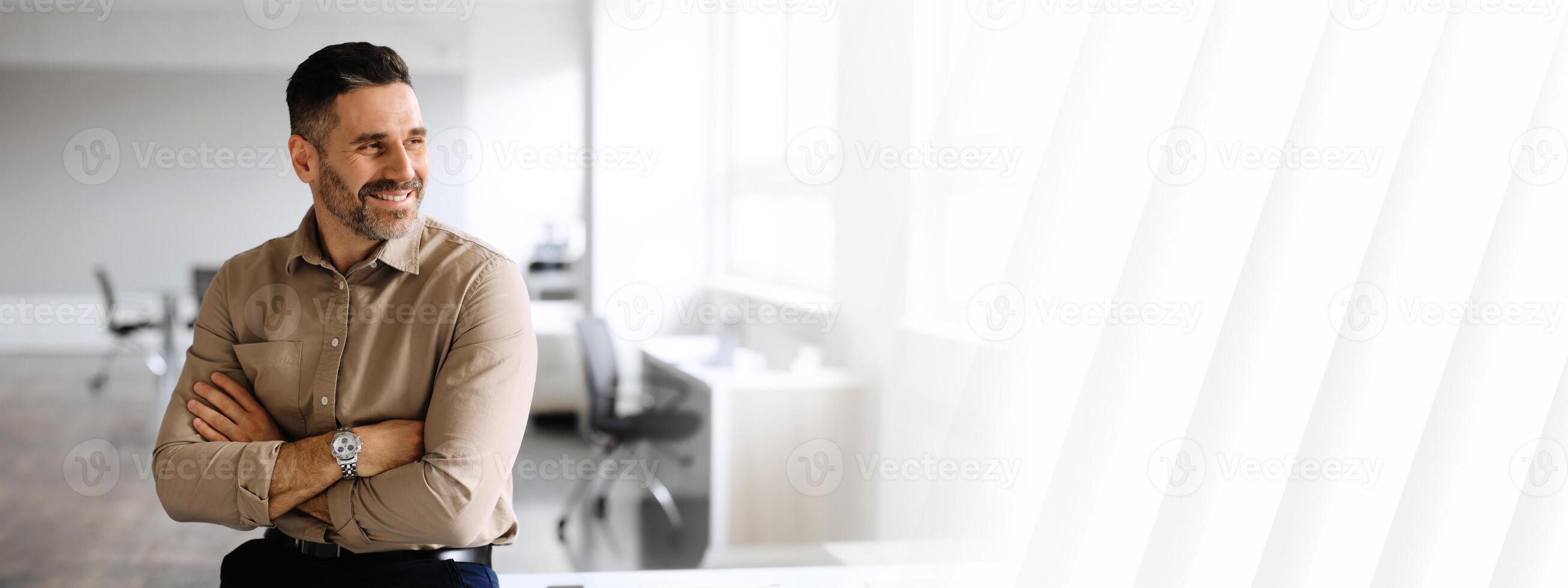 Successful middle aged businessman in shirt posing with crossed hands, looking away and smiling, working in light office interior, free copy space, panorama photo