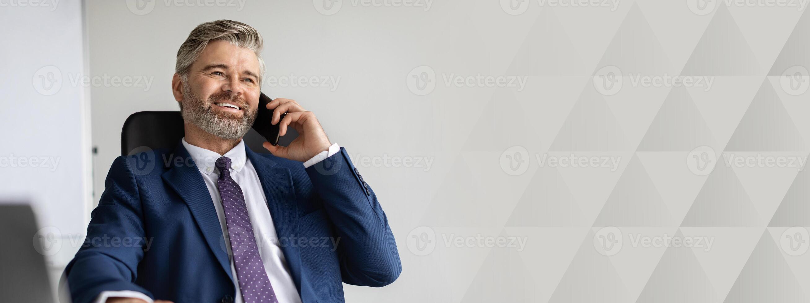 Successful Mature Businessman In Suit Talking On Mobile Phone At Office, Handsome Middle Aged Man Entrepreneur Sitting At Desk With Laptop And Enjoying Pleasant Call With Business Partner, copy space photo