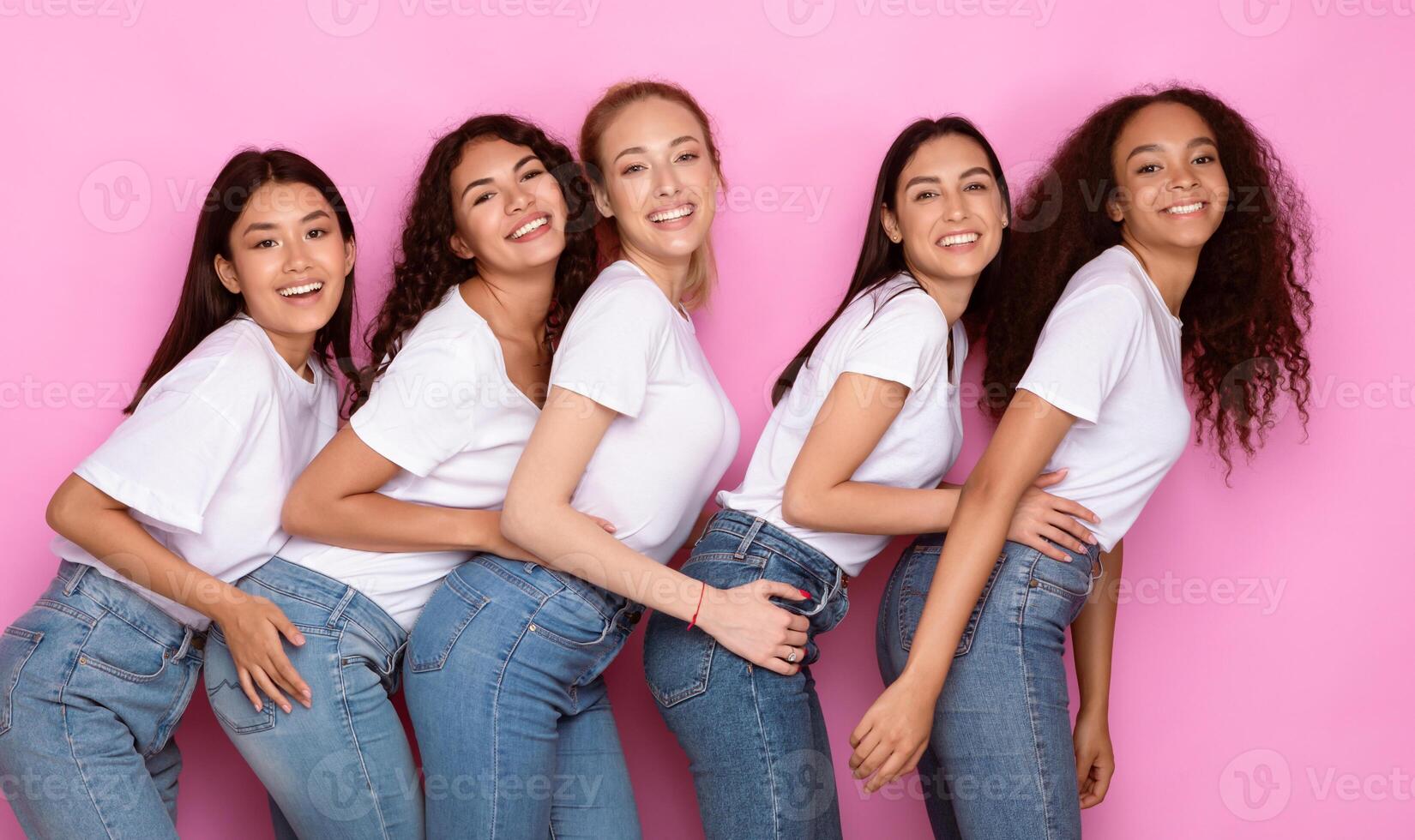 Five Multiracial Women Hugging Posing On Pink Studio Background, Smiling To Camera. Female Friendship Concept photo