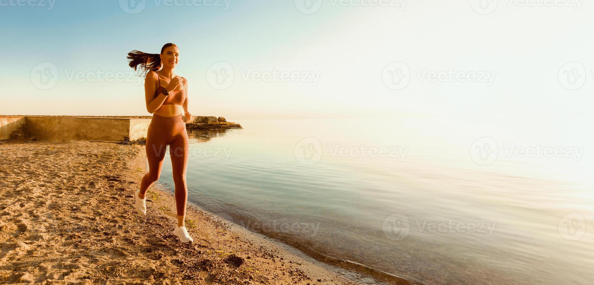 Morning Run. Cheerful active girl in sportswear running at the beach at the break of day, free space, banner photo