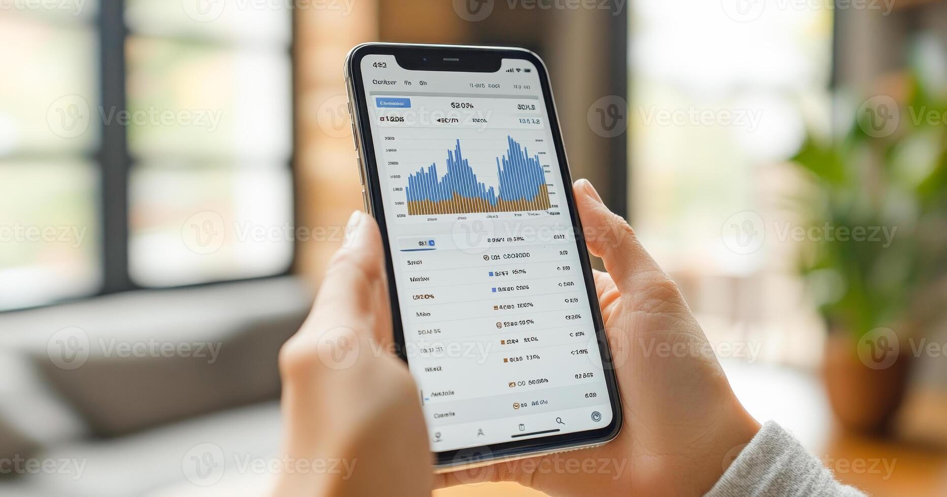 A person is holding a smartphone showing a detailed banking transaction screen with graphs and account statements. This activity takes place in a cozy indoor space with natural light. photo