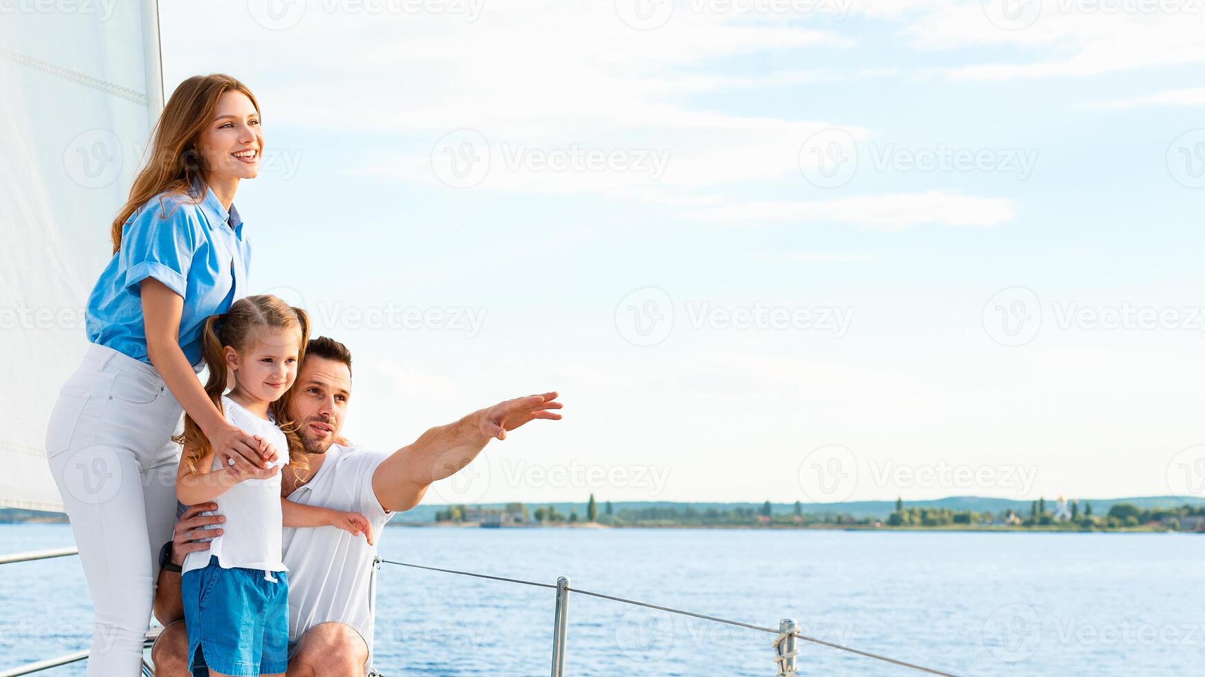 Sailing. Happy Family Embracing Standing On Yacht Looking And Pointing Aside At Sea Water Outdoors. Parents And Daughter Relaxing On Sailboat Enjoying Summer Weekend Together. Panorama, Copy Space photo