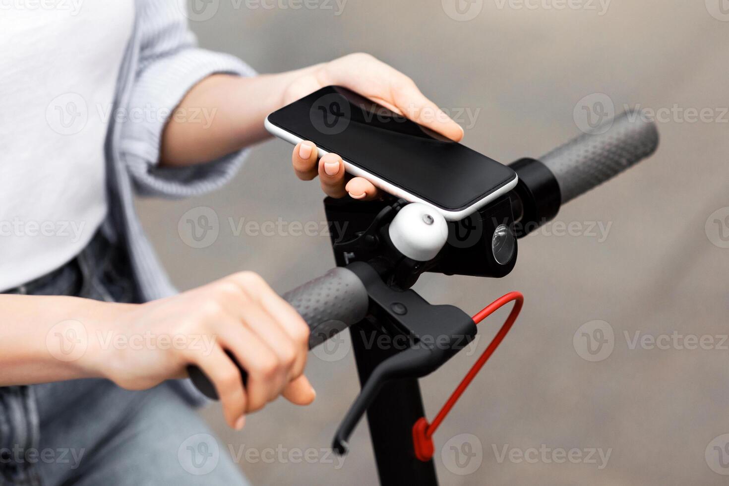 Electro-mobility Concept. Unrecognizable girl unlocking e-scooter using her smart phone with black blank screen, mock up photo
