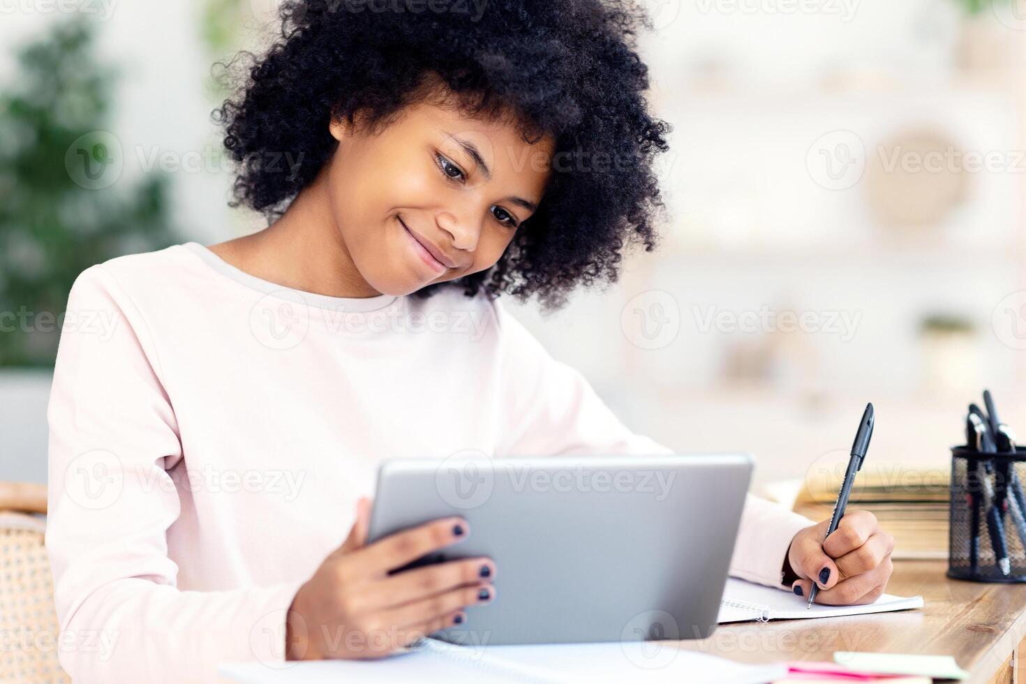 Happy Black Preteen Girl Using Tablet Computer Learning Online Doing Homework Sitting At Home. Distant Education photo