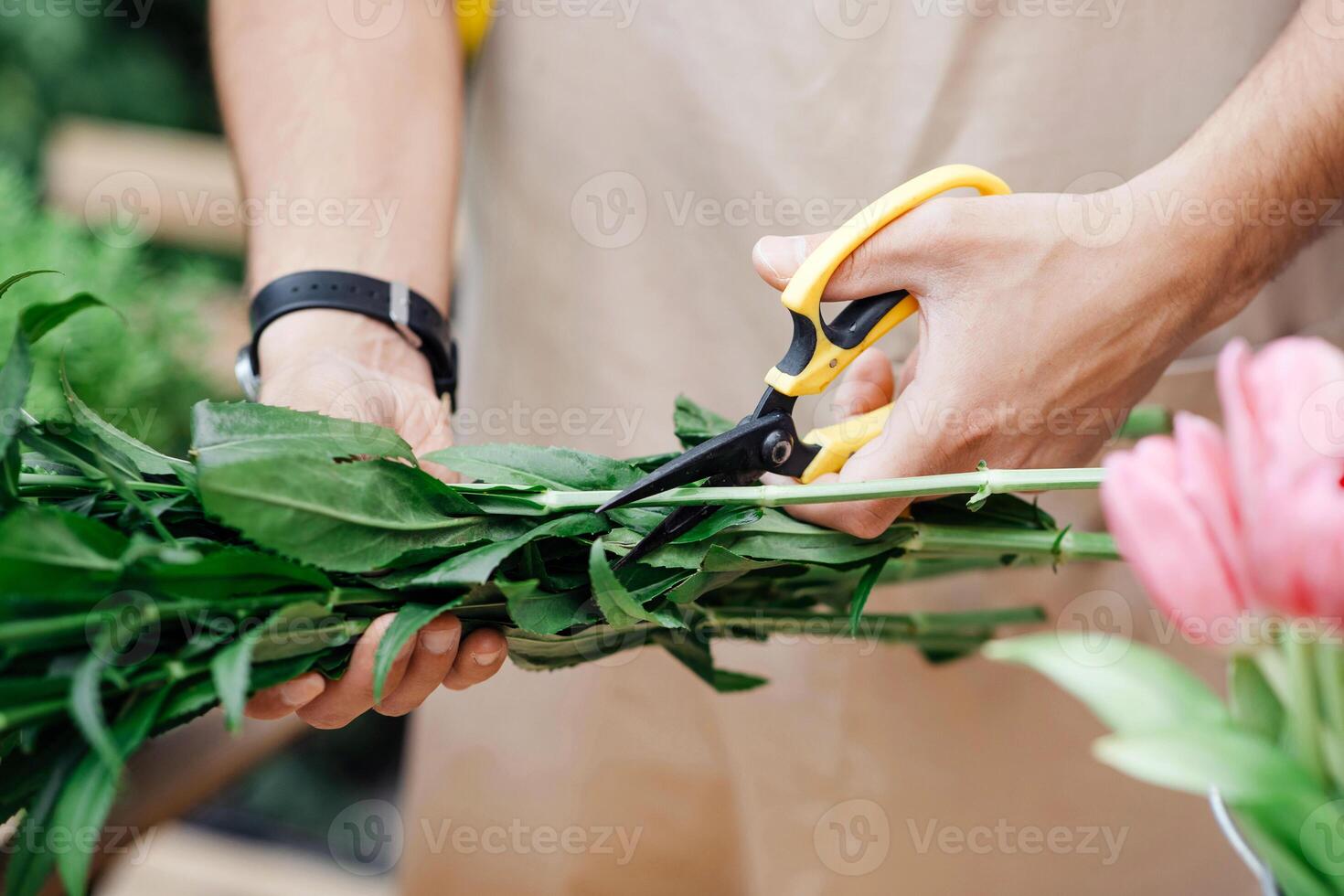 Covid-19 quarantine, ordering bouquets and delivery from flower shop. Young woman designer florist in apron with scissors cuts plants for composition with tulips in studio, close up, cropped photo