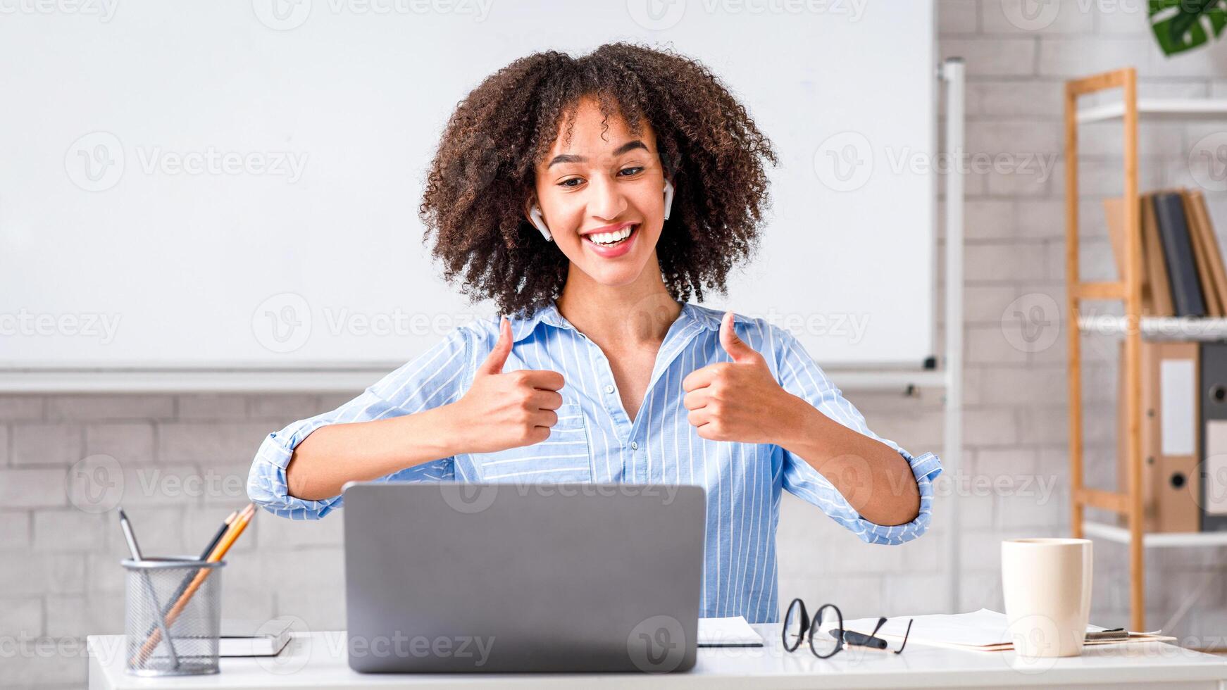 Excellent knowledge assessment. Cheerful african american lady showing thumbs up and communicating with students using laptop in classroom interior at home during covid-19 pandemic, copy space photo
