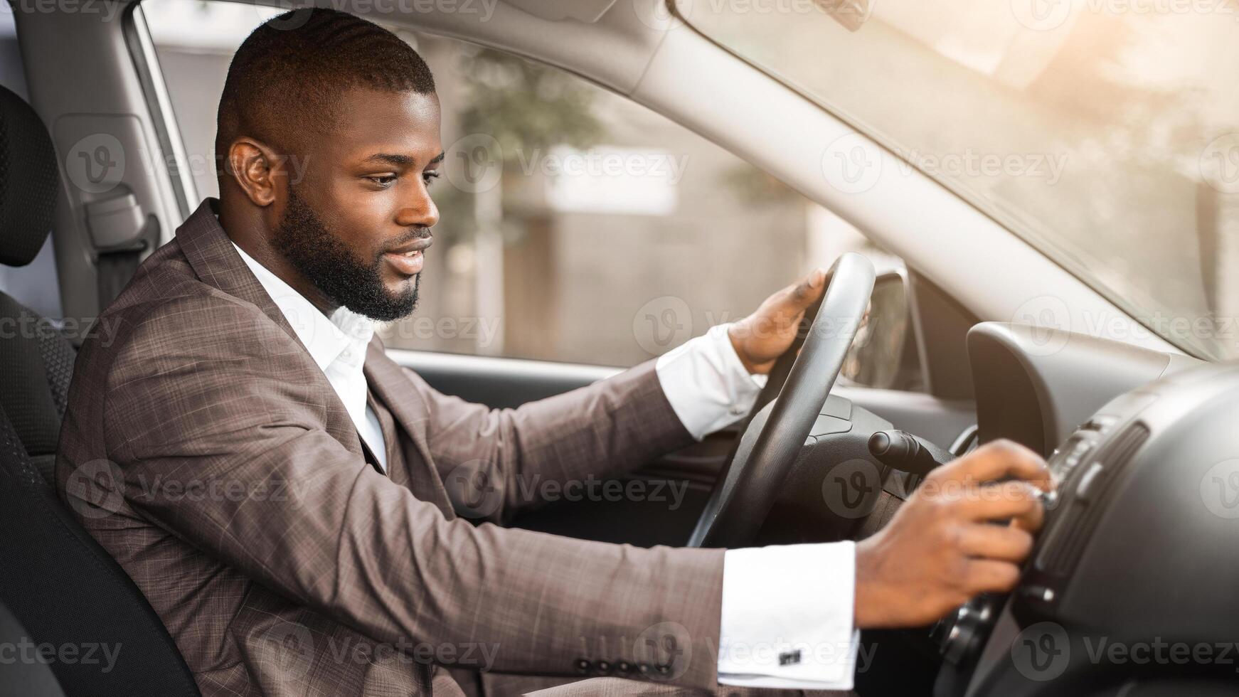 African american businessman turning on music in car before moving. Cheerful black businessman pushing button on functional panel in his car, turning on music before starting business trip photo