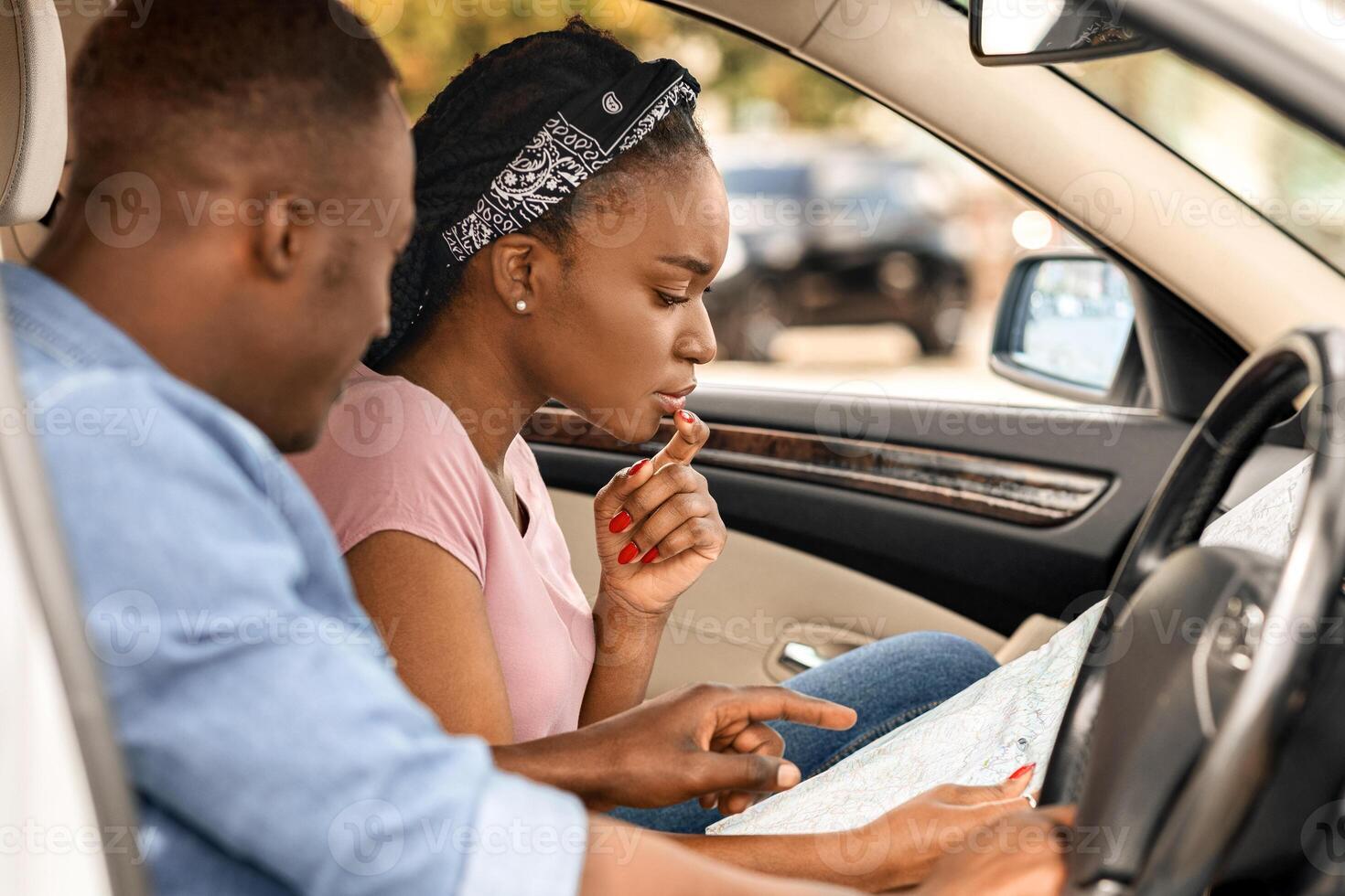 Afro american young couple travelling by car together, got lost, checking paper map, looking for appropriate way to destination, side view, copy space. GPS, location, map, navigation concept photo