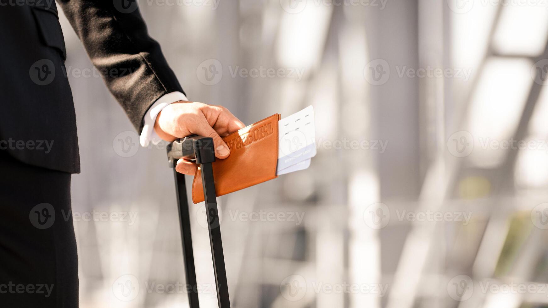Closeup of unrecognizable businessman holding passport and flight tickets, standing by window at airport with luggage, waiting for departure or taxi, going for business meeting, copy space photo