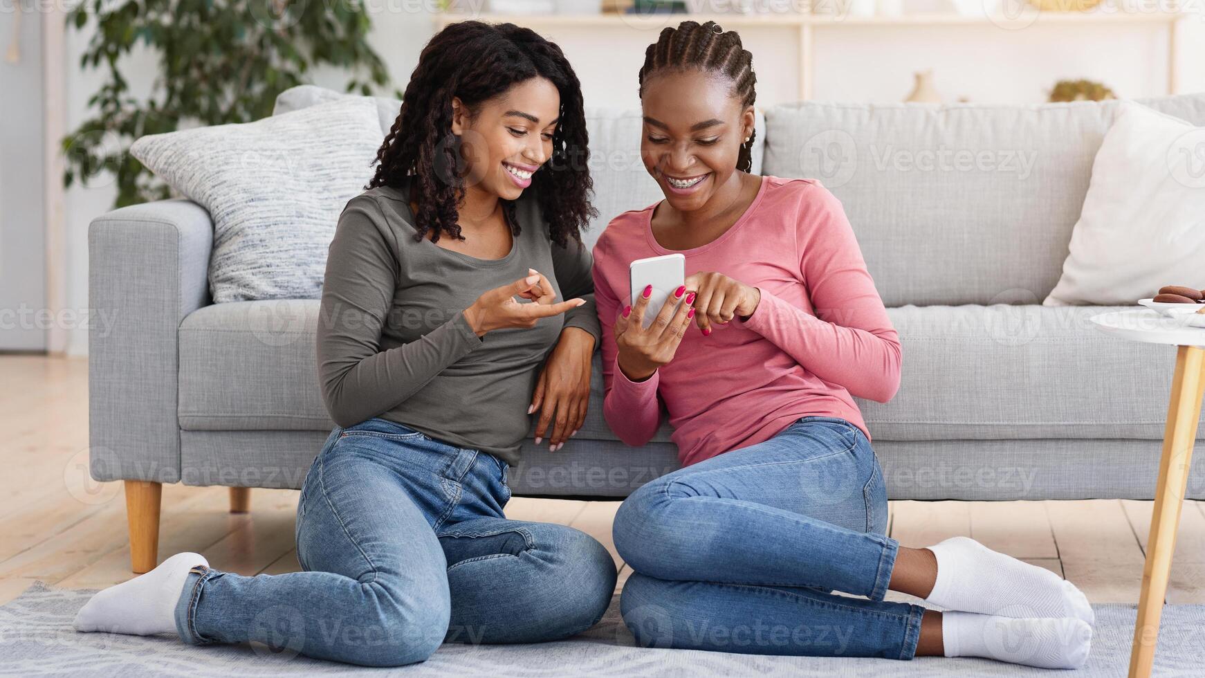 Happy black girls using new mobile app while resting at home together, free space photo