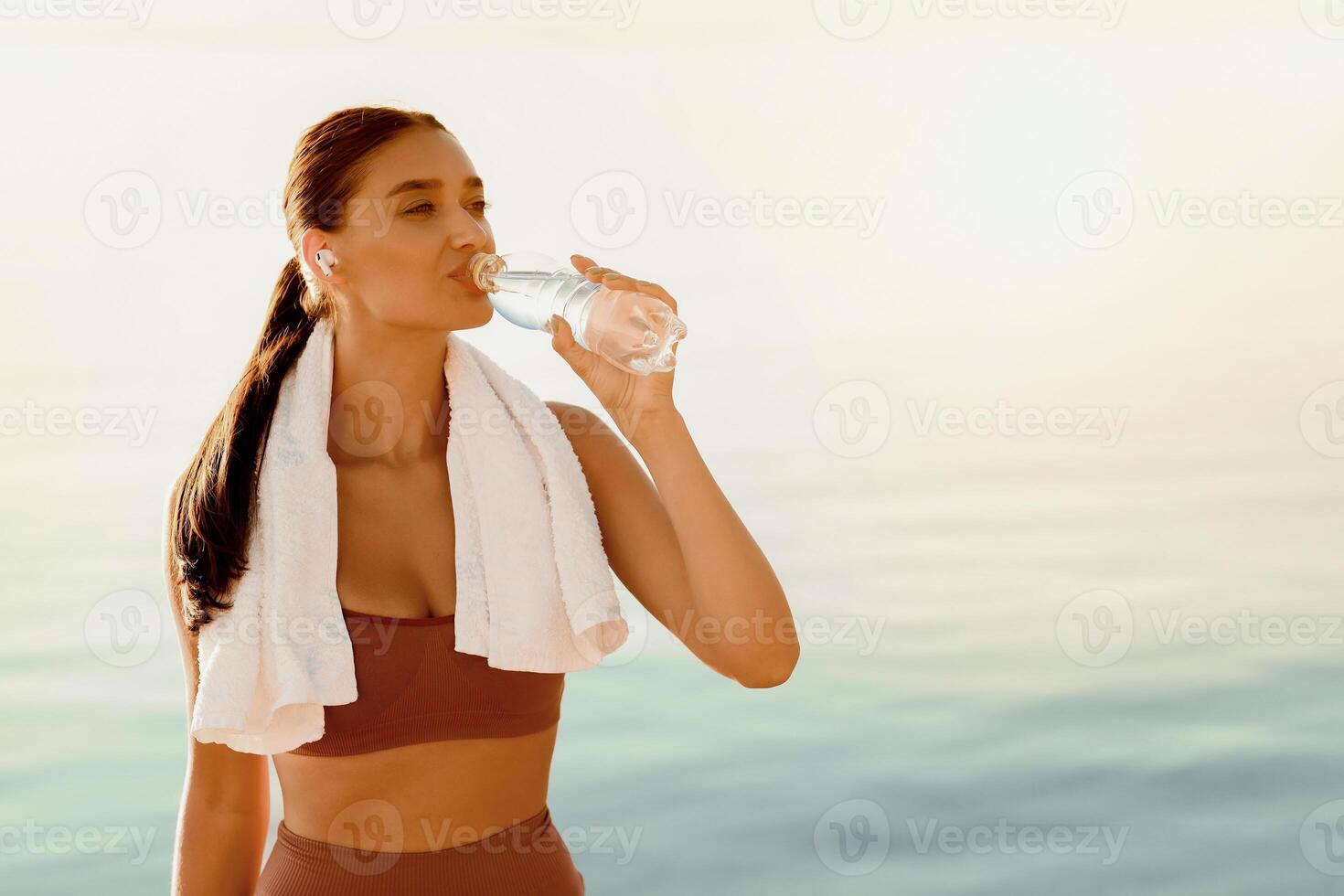 Sport And Hydration. Portrait of girl drinking mineral water from bottle, resting after training on beach, copy space photo