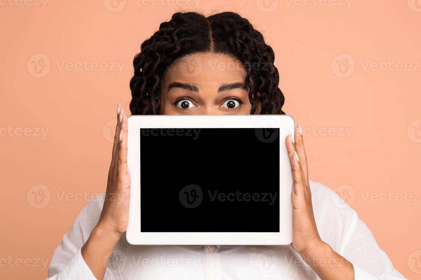 Black Girl Holding Digital Tablet With Blank Screen Near Face Advertising Website Posing On Beige Studio Background. Mockup photo