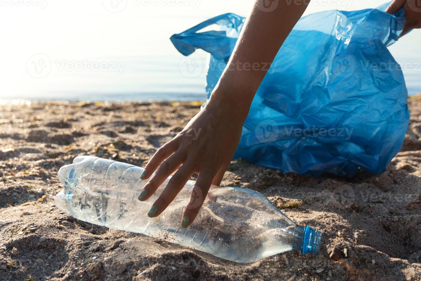 Volunteer Picking Up Wasted Plastic Bottle Cleaning The Beach Outdoor. Clean The Ocean Concept. Background With Copy Space photo