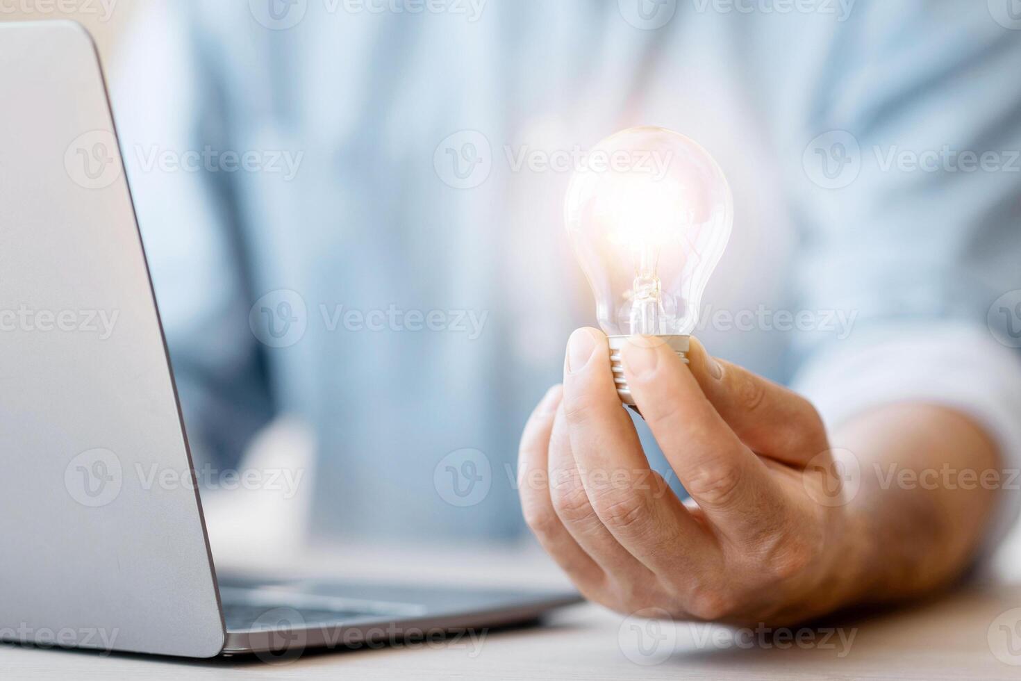 Idea Concept. Unrecognizable businessman holding illuminated light bulb at workplace in office, got business solution, closeup photo