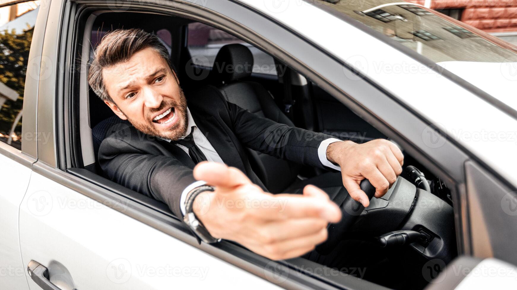Mad businessman driving luxury car, stuck in traffic, late to airport, copy space. Furious middle-aged man in expensive suit screaming and gesturing to other drivers while driving auto photo