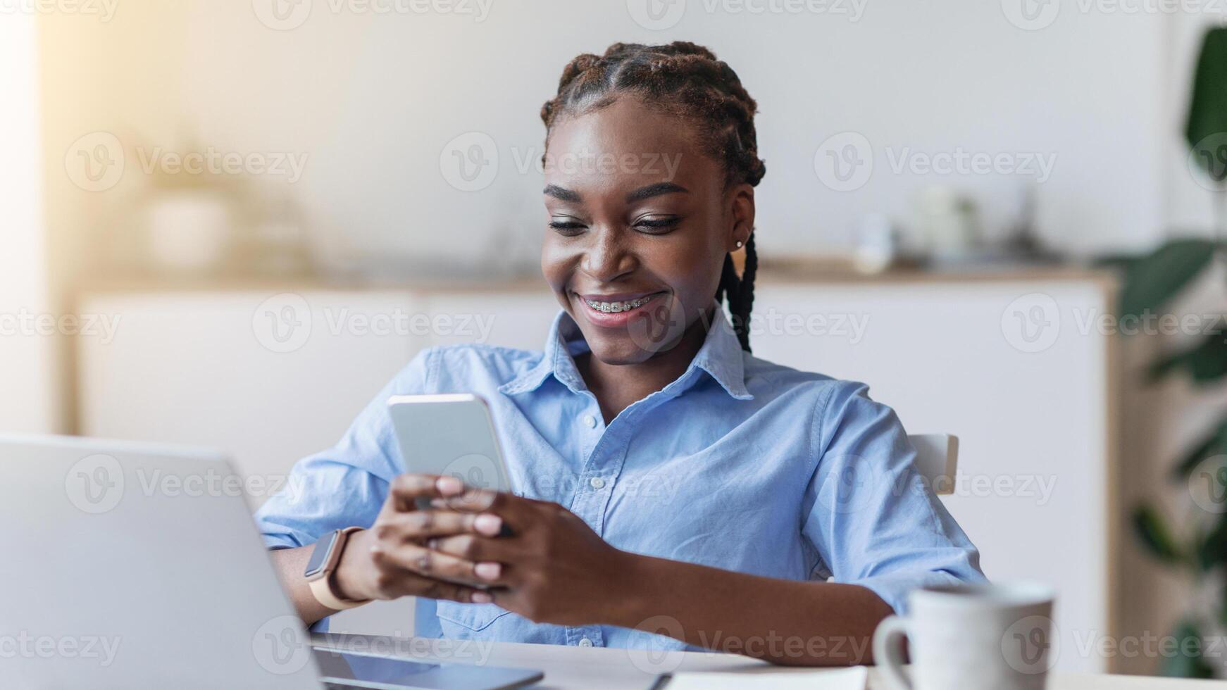 Black female employee using mobile phone at workplace in office, checking social media on smartphone during break at work, copy space photo