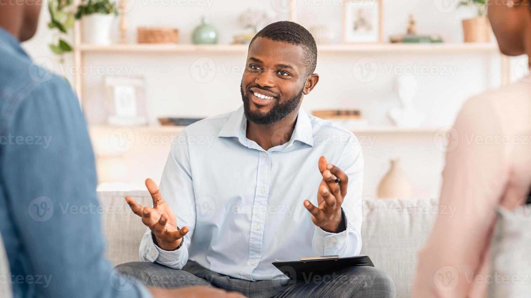 Confident black family counselor talking with married couple, giving advice in his office, selective focus with free space photo
