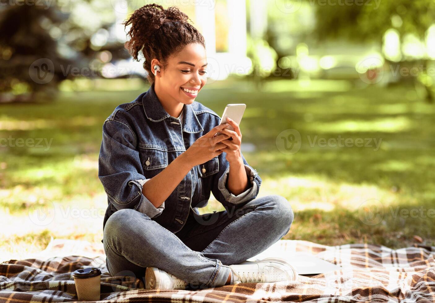 Cheerful African American Lady Using Smartphone Texting In Social Media Mobile App Sitting In Park Outside. Online Communication Applications Concept. Free Space For Text photo