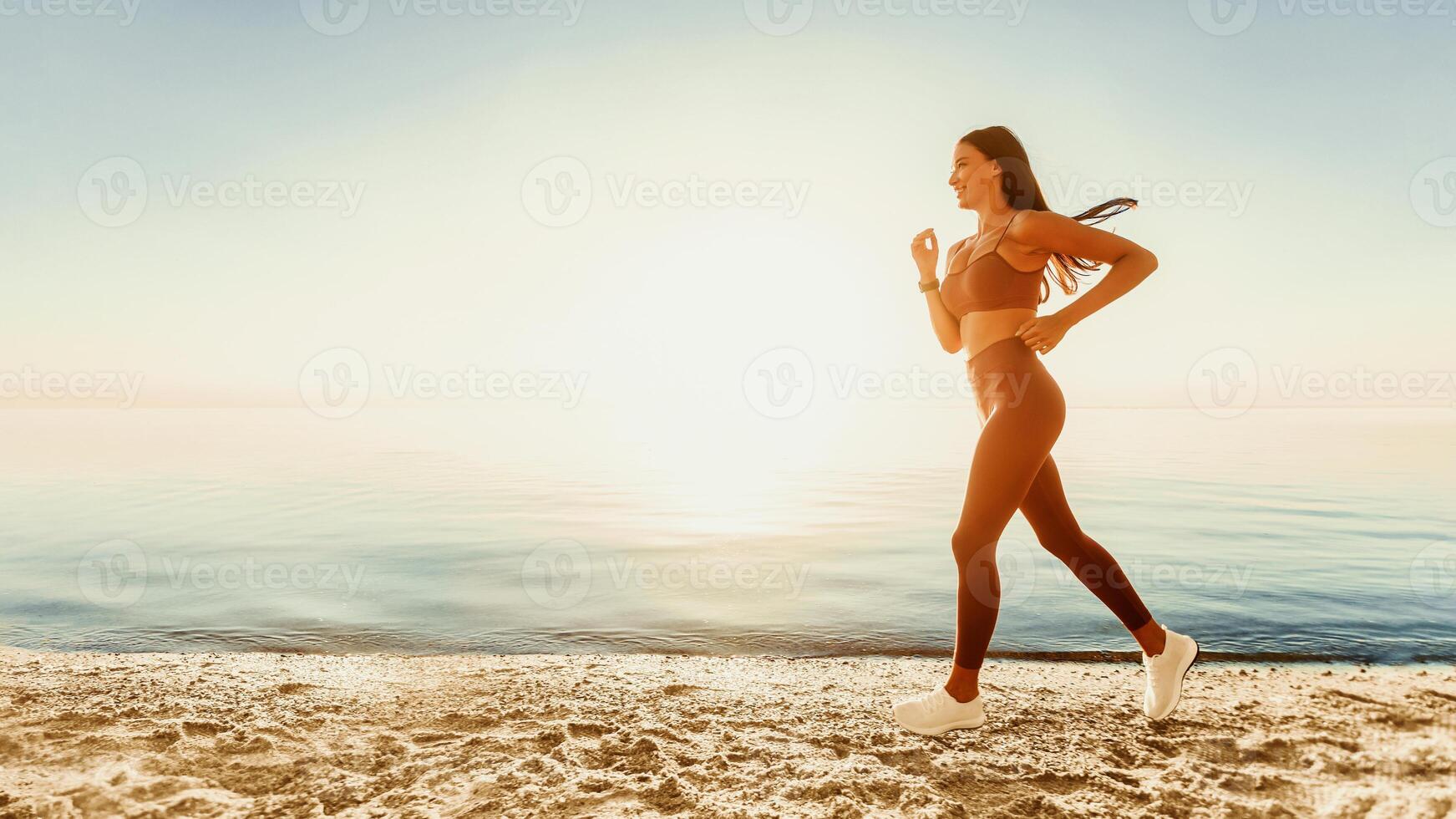 Side view of smiling woman running on the beach over natural warm sunrise background, copy space, panorama photo