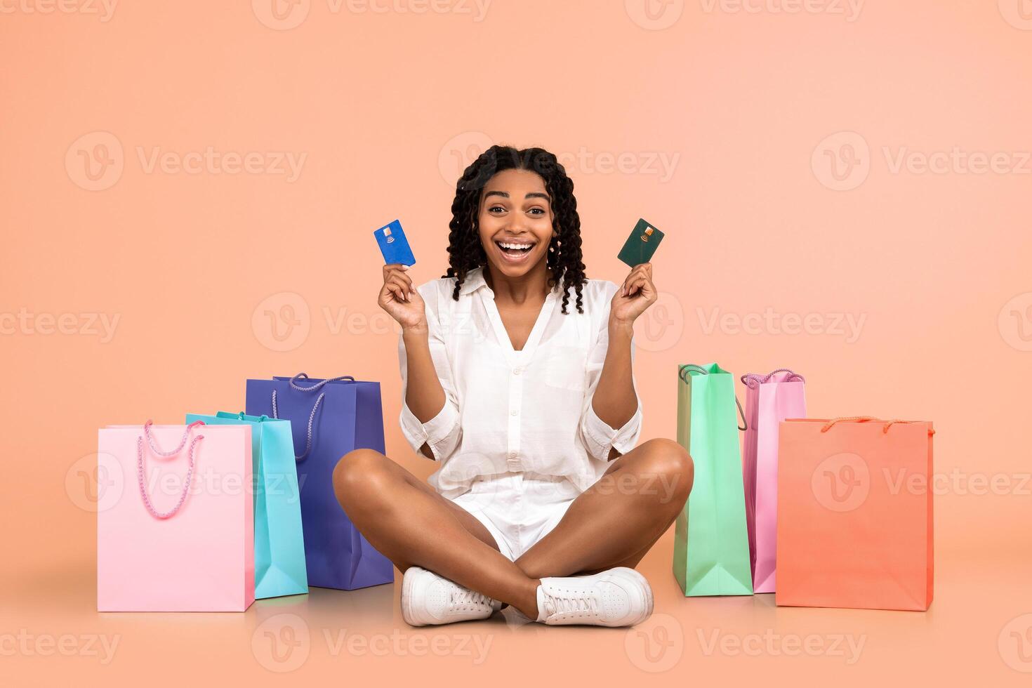Shopping Budget. Joyful African American Woman Buyer Holding Credit Cards Sitting Among Shopper Bags In Studio On Beige Background photo