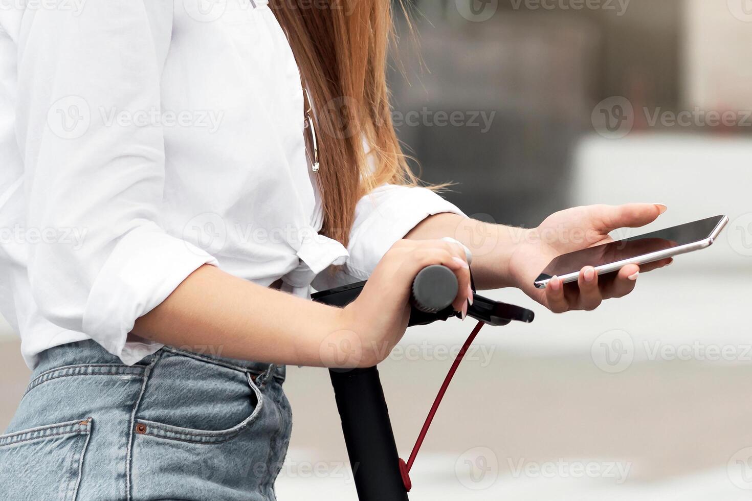 Portrait of smiling trendy couple using smart phones and stand-up scooters, looking at camera photo