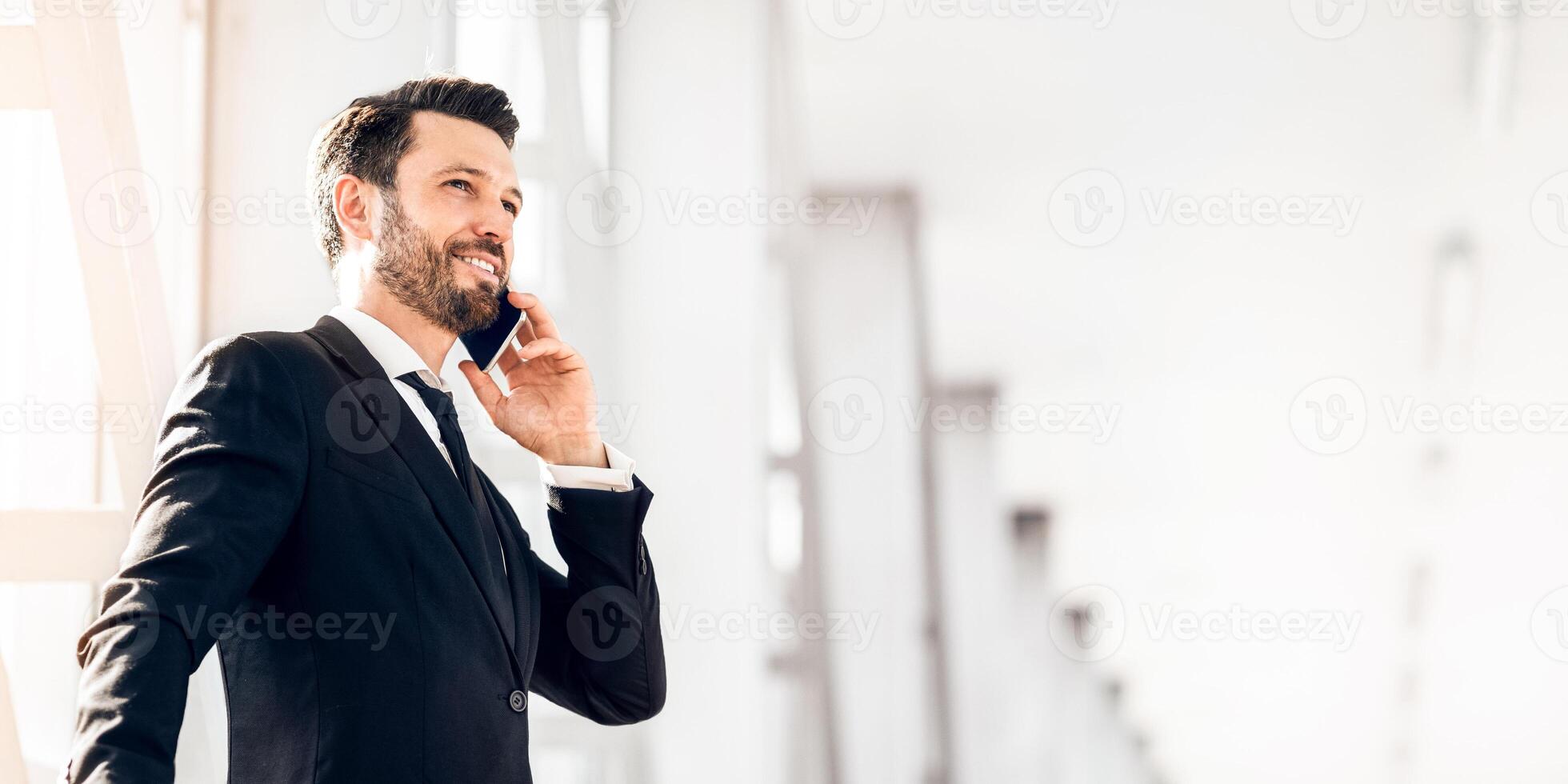 Happy wealthy businessman standing in airport, talking on phone, having business trip, panorama with copy space photo