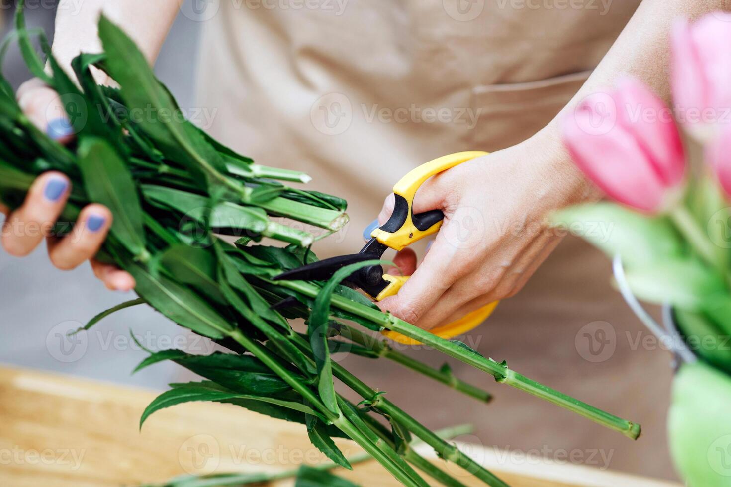 Creative designer in flower shop, small business owner works outdoor. Millennial female in apron makes bouquet, forms tulips for client, on plants studio outdoor background, cropped, close up photo
