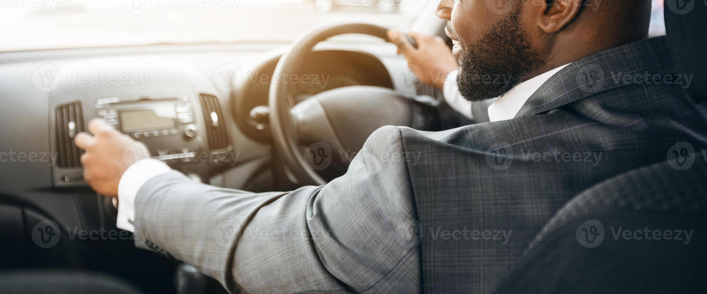 African american businessman turning on music in car before moving. Cheerful black businessman pushing button on functional panel in his car, turning on music before starting business trip, copy space photo