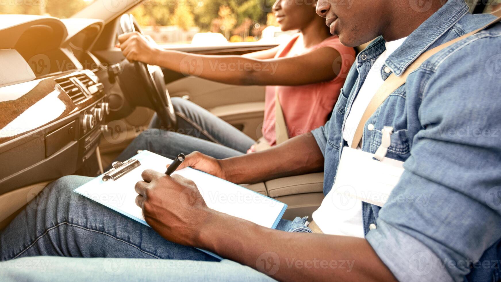 Male instructor examining black woman driving car, sun flare, driving school concept photo
