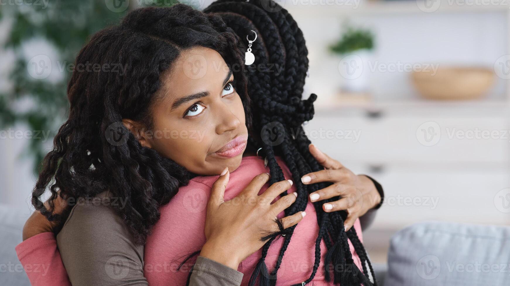Irritated black lady hugging her girlfriend with annoyed face expression, fake friendship concept. Two african american women embracing, crying lady looking for support, copy space photo