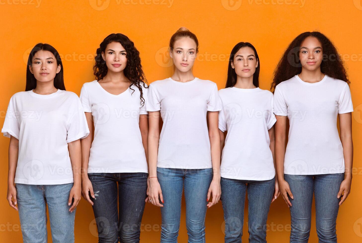 Five Serious Multiethnic Women Standing Together In A Row Looking At Camera In Studio Over Yellow Background. Female Millennials Posing In Studio. Unity And Diversity Concept photo