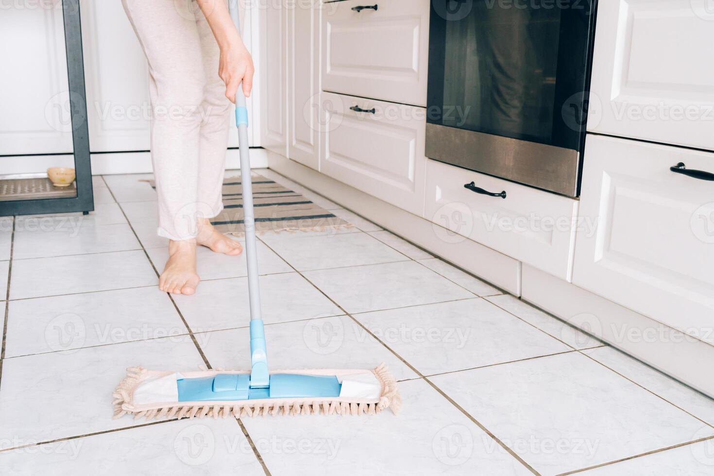 Female adult cleaning kitchen floor with mop photo